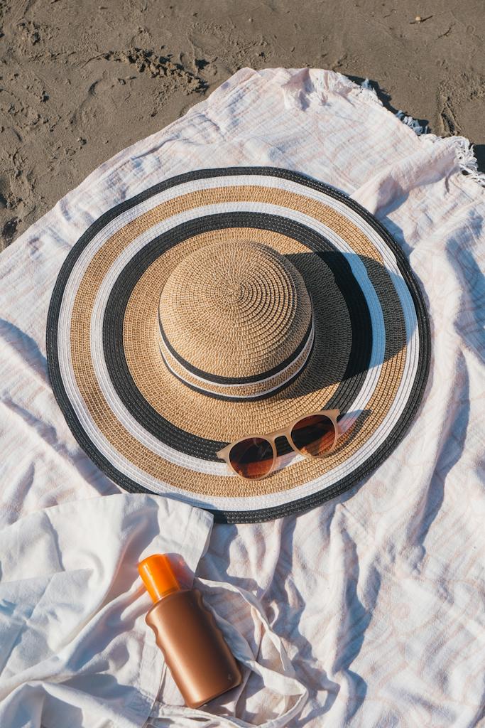 A Hat, Sunglasses and Sunscreen on a Blanket on the Beach